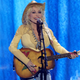 A photo of Dolly Parton on stage in a yellow outfit playing the guitar.